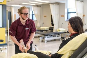 Étudiant en physiothérapie prodiguant des soins à la cheville d'une autre étudiante