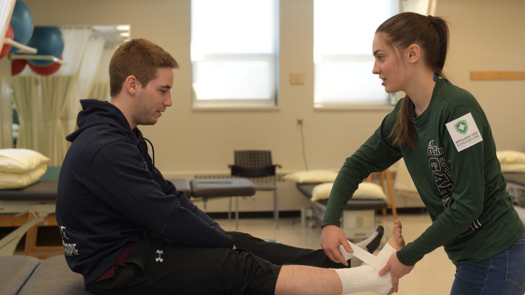 Étudiante faisant un bandage au pied d'un autre étudiant